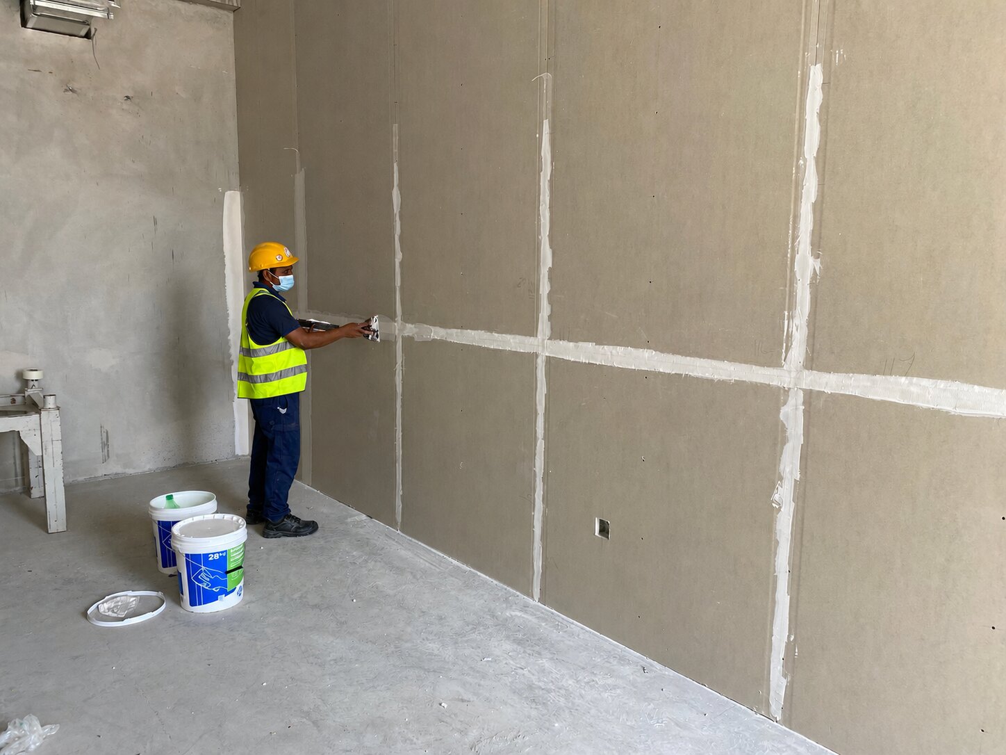 Worker in safety equipment jointing a gypsum partition wall